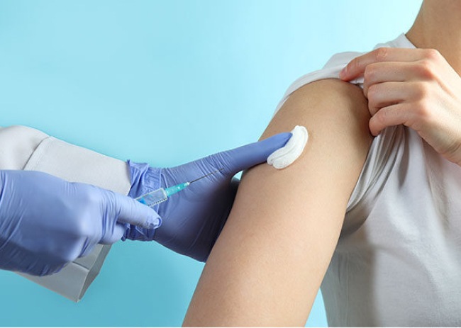 The image shows a doctor administering an injection to a woman’s arm.