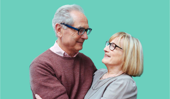 An image of an elderly man holding an elderly woman in his arms as they smile and gaze at each other.